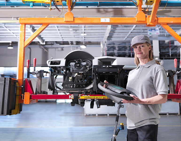 young lady holds steering wheel in car assembly plant